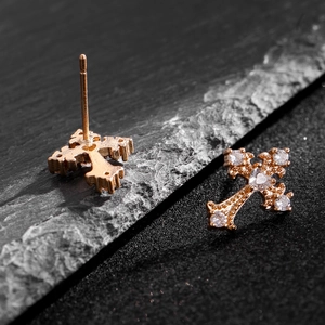 Dettaglio macro di orecchini a croce gotici dorati con zirconi scintillanti su fondo di pietra