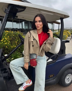 Short khaki trench jacket styled with red polo shirt and chain bag on a golf cart