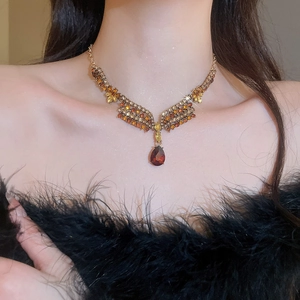 Close-up of a vintage floral necklace with red teardrop gemstone on a female model