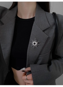 Silver sunburst brooch with cubic zirconia crystals worn on a dark grey blazer lapel