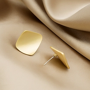 Minimalist geometric square matte gold stud earrings on champagne silk fabric background