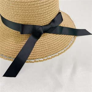 Detail of straw hat featuring black ribbon bow and delicate white lace edge trim