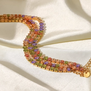 Nahaufnahme der dreilagigen Goldarmkette mit bunten Zirkonia auf weißer Seide