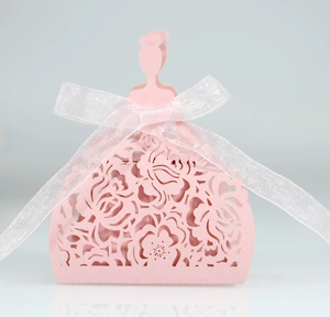 Detail of pink laser-cut dress-shaped favor box with intricate floral patterns and white ribbon