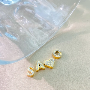 Macro shot of gold-plated alphabet S, A, G and heart charms with pavé cubic zirconia