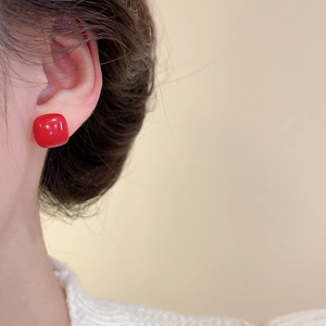 Close-up of a model wearing square red resin stud earrings with a glossy finish