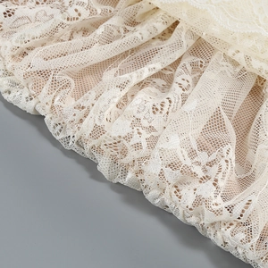 Macro shot of delicate floral lace embroidery and pleated details on a cream party dress