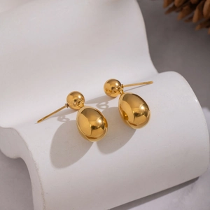 Macro shot of gold teardrop earrings with mirror finish on white curved stand