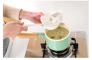 Wheat straw slotted spoon scooping food from a pot in a bright modern kitchen