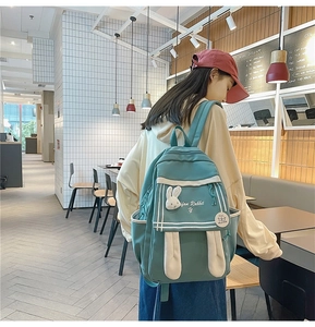 Girl wearing a cute blue-green school backpack with long rabbit ears in a cozy cafe