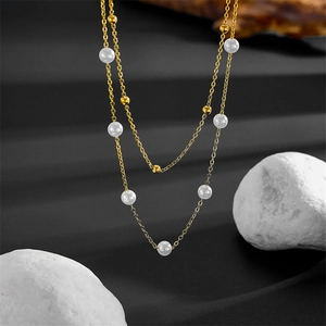 Elegant double-layered gold chain necklace with white pearls on a dark background