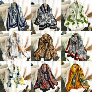 Nine elegant long satin scarves with diverse floral and geometric patterns on a beige chair