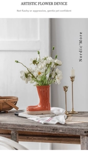 Creative orange rain boot ceramic vase with white daisies on vintage wood table