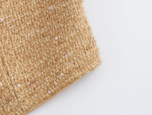 Close-up detail of beige and gold tweed fabric texture with shimmering sequins on the set