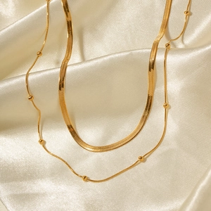 Detailed shot of double-layer gold snake and bead chain necklace on silk fabric