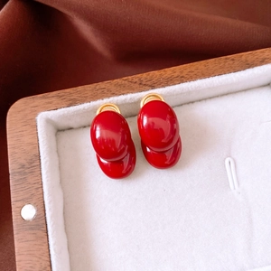 Detail view of oval dark red stud earrings in gold base on white jewelry box padding