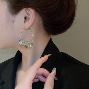Detail of silver hoop earrings with metallic sequin tassels worn by a model in a close-up