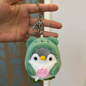 Cute plush penguin keychain wearing a green frog costume and holding a pink lollipop