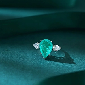 Macro shot of 925 silver ring featuring a pear-cut emerald gemstone on green velvet