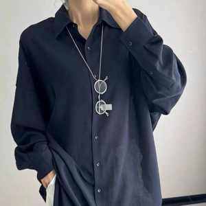 Detail of minimalist long necklace with metal eye pendant over a navy blue shirt fabric