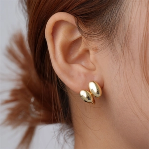 Detail of polished gold irregular double-bean earrings worn on a model's earlobe
