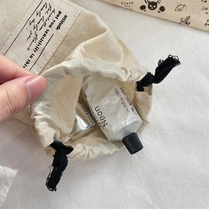 Close-up of cotton drawstring bag with printed label holding cosmetics and hand cream