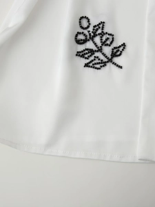 Macro detail of black beaded floral embroidery on white long-sleeve women shirt