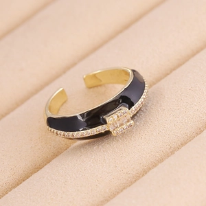 Anello geometrico dorato con smalto nero e zirconi incastonati, design a fibbia
