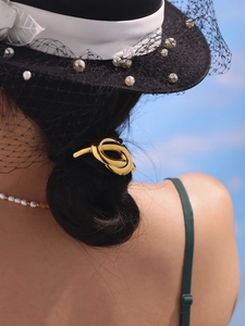 Detail of a minimalist gold metal knot ponytail holder on a model's hair