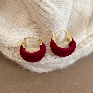 Detailed view of burgundy velvet semi-hoop earrings on warm knit fabric background