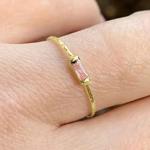 Macro shot of minimalist gold ring with rectangular pink zircon on finger detail