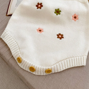 Détail d'un barboteuse en maille pour bébé avec broderie de marguerites et boutons