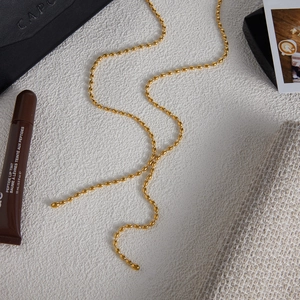 Polished gold beaded Y-chain necklace styled with premium accessories on a textured surface