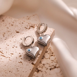 Silver stainless steel heart hoop earrings with blue evil eye charm on beige stone