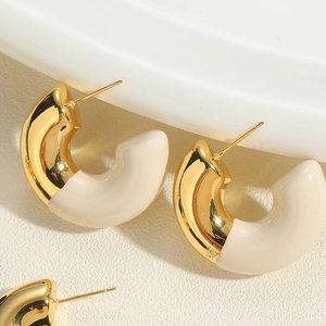 Macro shot of C-shaped gold earrings with cream enamel and S925 sterling silver stamp