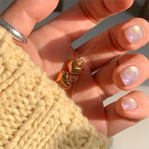 Macro shot of gold heart-shaped stud earrings held against a cozy beige knit sweater