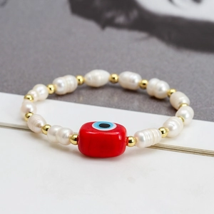 Detail view of freshwater pearls and golden beads bracelet with a red evil eye charm