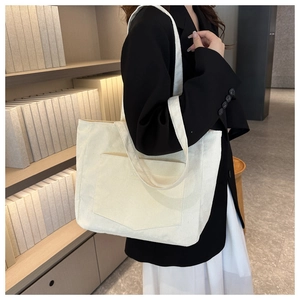 Detail of cream corduroy tote bag with front pocket shown on a model in a minimal setting