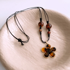 Detail of amber tortoiseshell flower pendant on a woven cord necklace in a ceramic tray