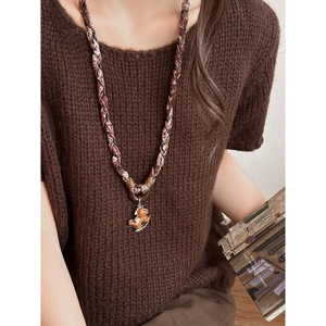 Gros plan du collier vintage en tissu avec pendentif cheval à bascule sur un pull marron