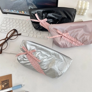 Detailed view of glossy bow pencil cases in black, pink, and silver on a modern desk