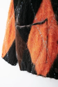 Gros plan d'un pull en maille à losanges orange, noir et marron avec texture peluche