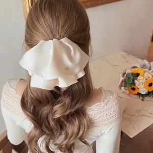 Elegant white satin double-layered bow hair clip with gold metal logo on female model