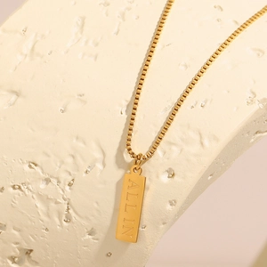 Macro detail of 18K gold-plated box chain with square pendant engraved with ALL IN