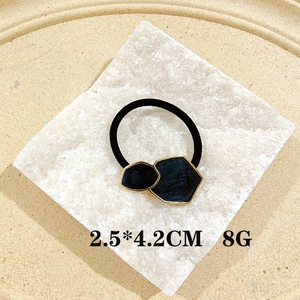 Detail view of black geometric hair tie with gold trim on a white stone background