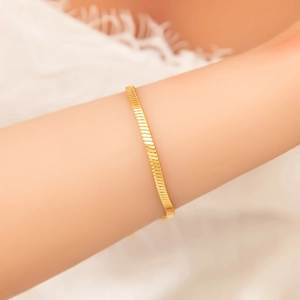 Detail of 18k gold plated flat snake bone chain bracelet worn on a woman's wrist