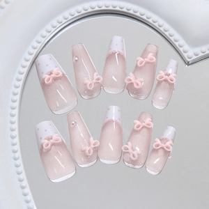 Pink press-on nails with white polka dots, 3D bows, and pearls on a mirrored surface