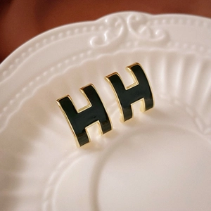 Macro detail of H-shaped black enamel stud earrings with gold plating on a ceramic plate