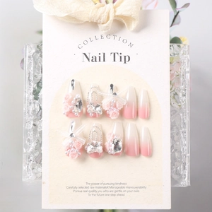 Close-up of pink gradient press-on nails with resin roses, pearls, and bows on a display card