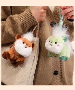 Detail of plush pony keychain charms in brown and green hanging on a beige canvas bag